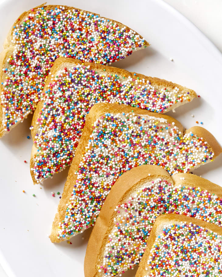 Overhead shot of five diagonal slices of fairy bread on a white oval platter.
