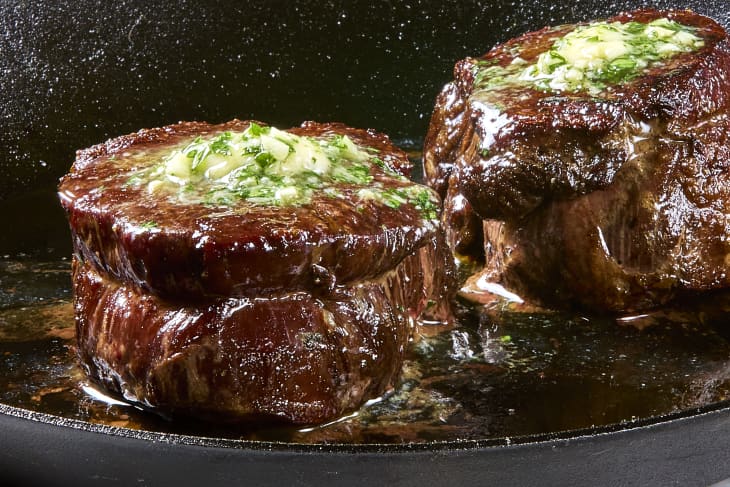 Head on shot of seared filet mignon topped with butter in a pan.