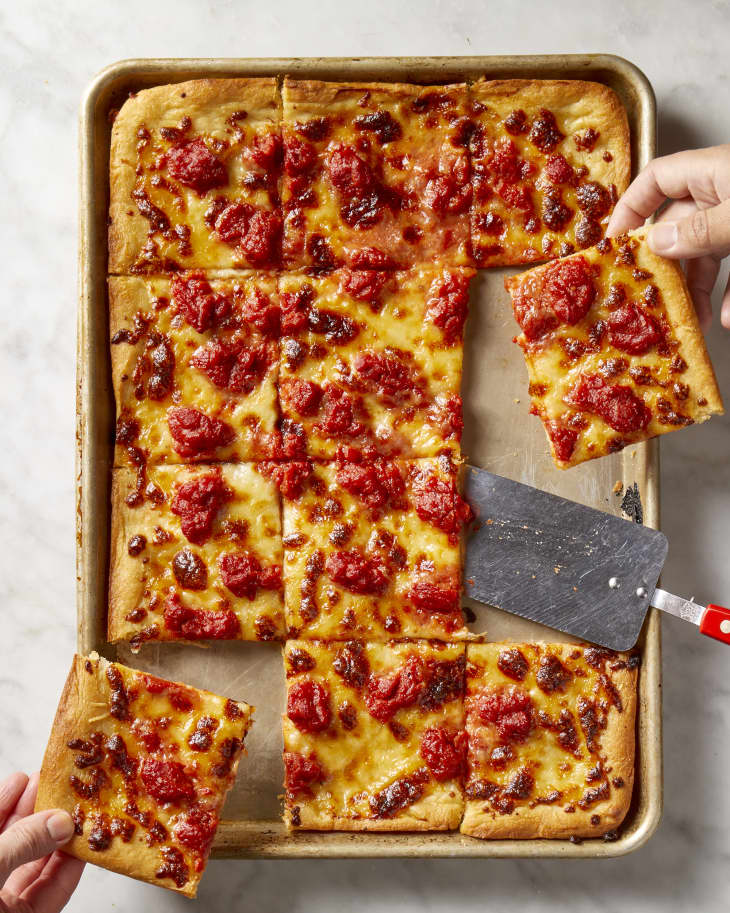 a hand reaching in and pulling out a slices of pizza from the sheet pan.