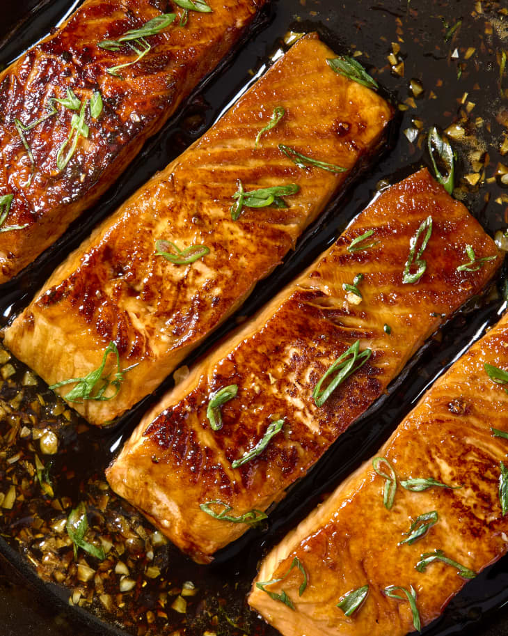 Overhead shot of four cooked pieces of salmon in a cast iron, topped with green onion.