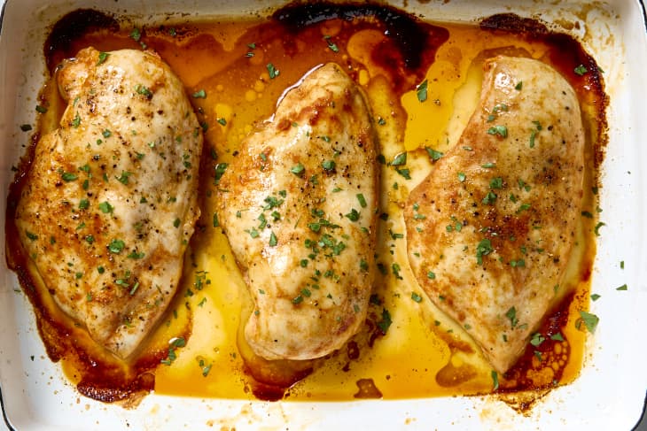 Three baked chicken breasts in a baking dish, topped with parsley.
