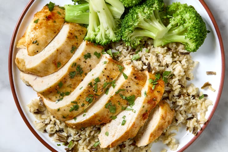 sliced chicken breast on a plate over brown rice with steamed broccoli.