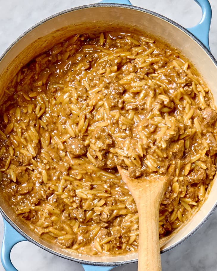 Overhead shot of creamy beef and orzo in a light blue pot, with a wood spoon stirring it.