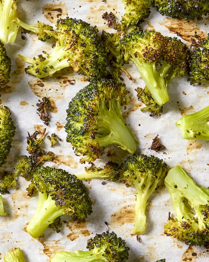 Overhead shot of roasted broccoli on white parchment paper, in a sheet pan.