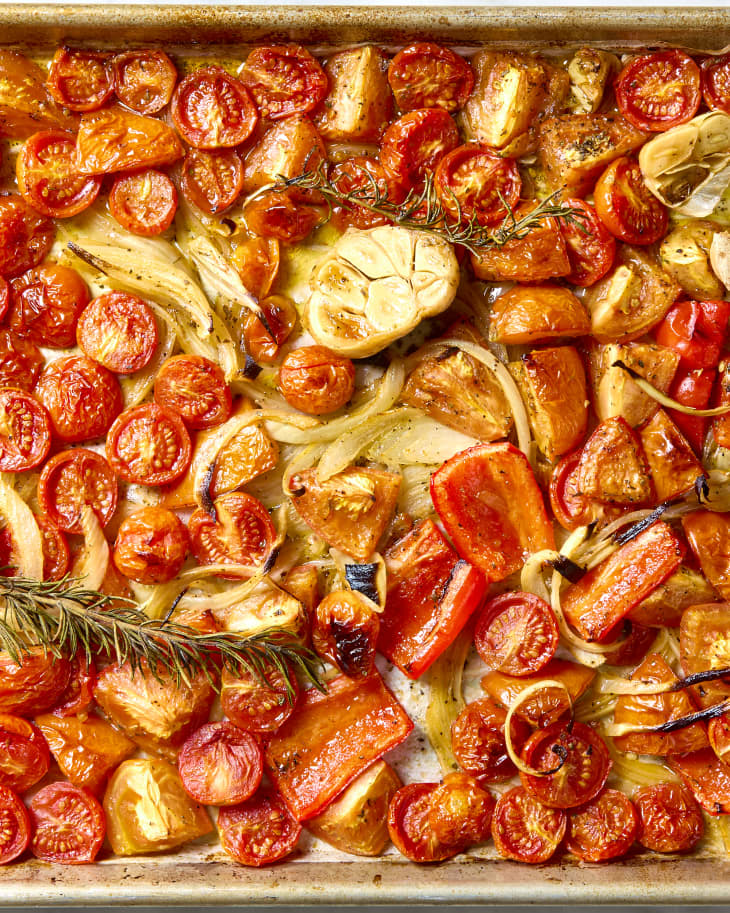 Overhead shot of roasted tomatoes, garlic and onions on a baking sheet.