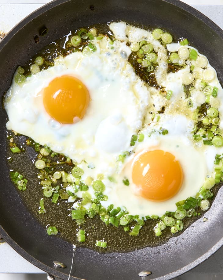 Overhead shot of two fried eggs in a pan with scallions.