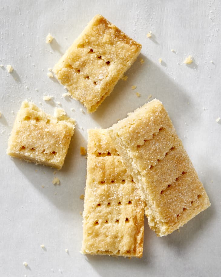 Overhead shot of two shortbread cookies stacked on each other and a third, broken cookie above the on white parchment paper.