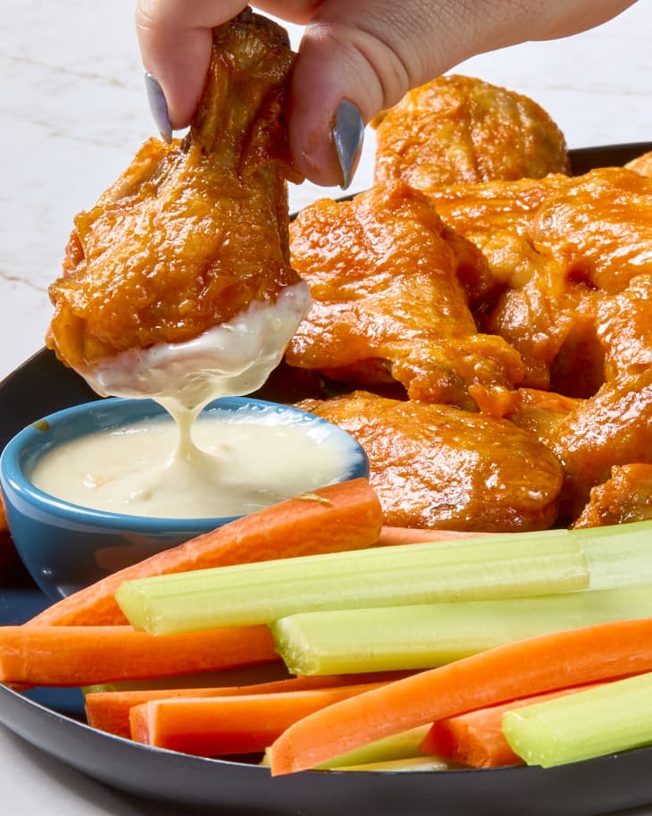 head on shot of a hand holding a buffalo wing and dipping it into the ranch.