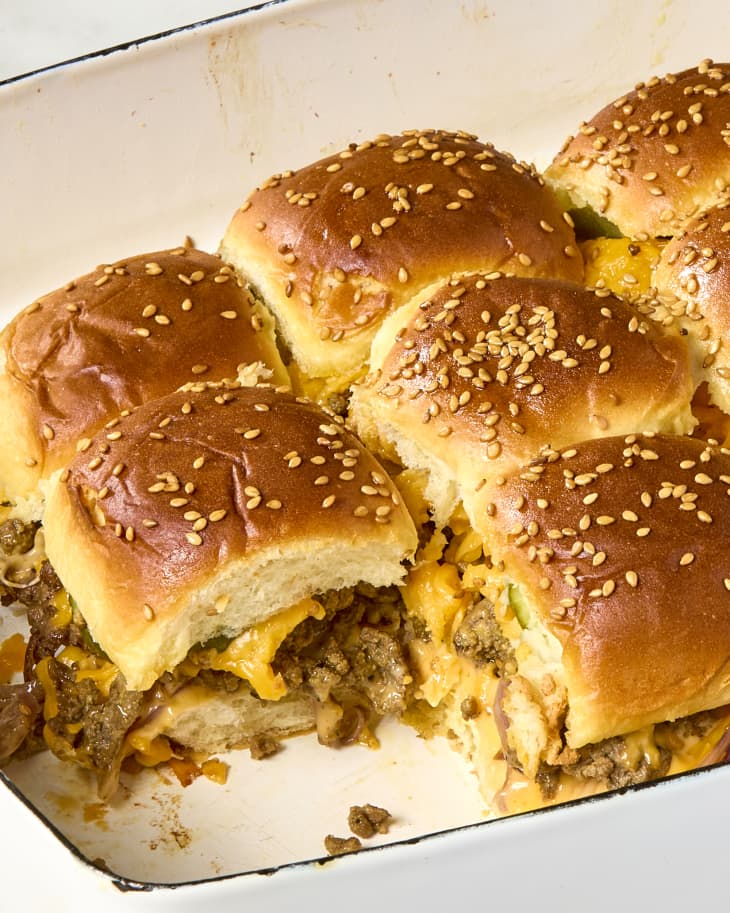 close up shot of a tray of cheeseburger sliders in a white pan, with one slider taken from it.