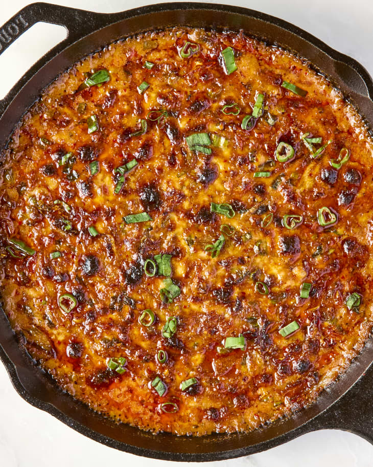 overhead shot of cheesy kimchi dip baked in a cast iron pan, topped with chives.