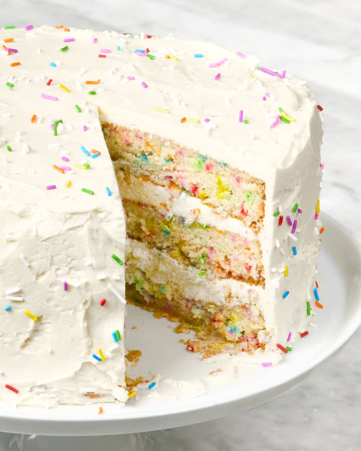 head on shot of a whole funfetti cake with a single slice taken from it.