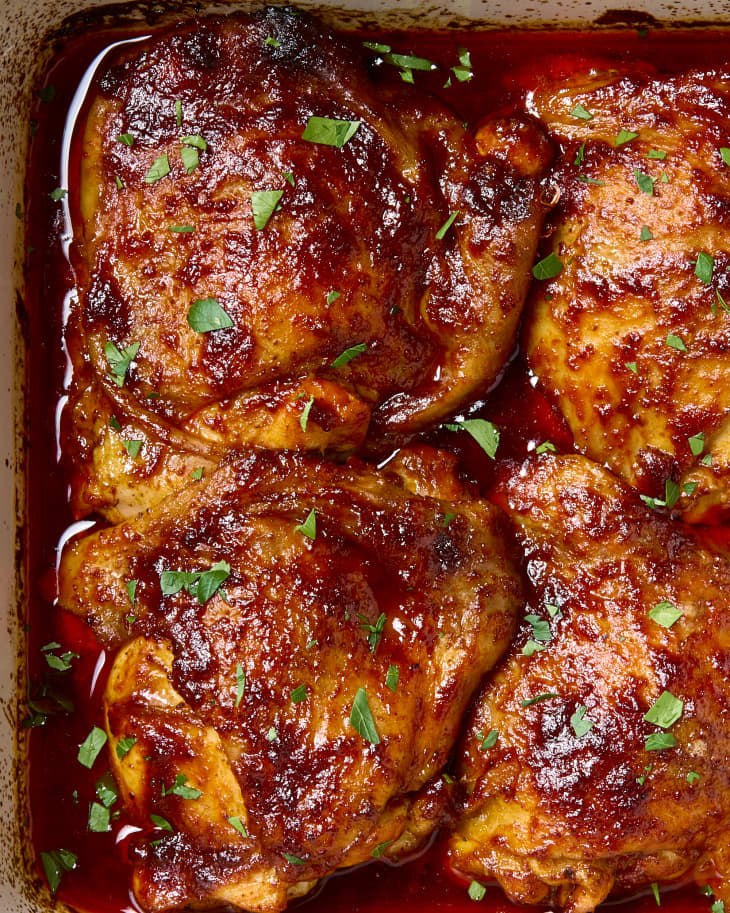 close up shot of four harissa orange chicken thighs in a small white baking dish.