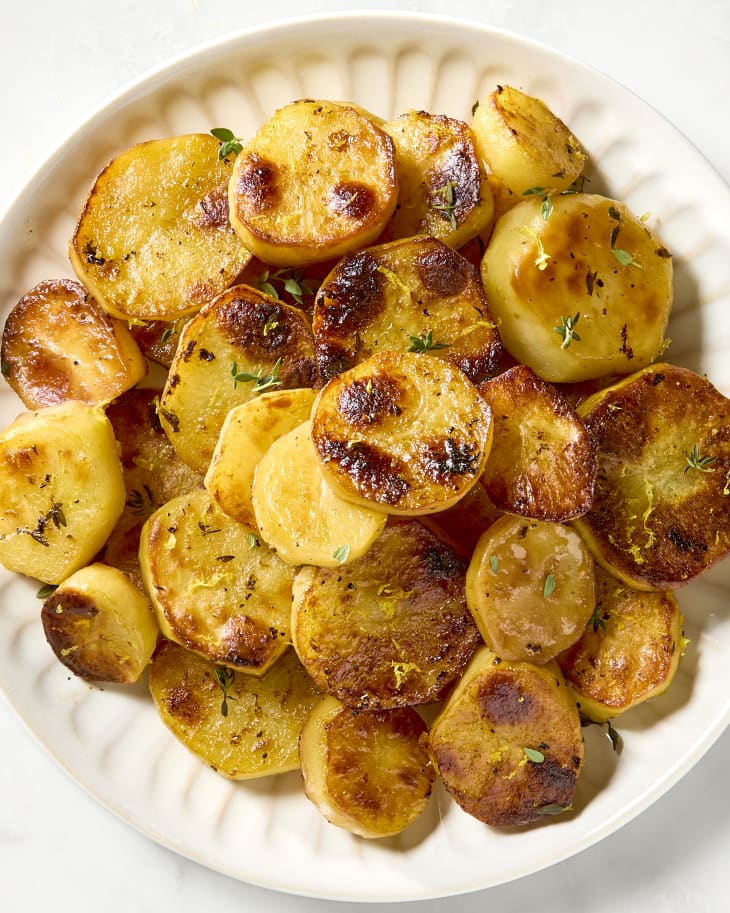 overhead shot of lemon butter potatoes on a white plate topped with herbs.