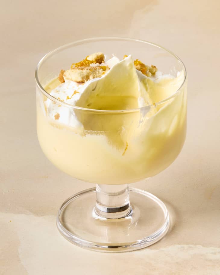angled shot of a single dessert glass with orange creamsicle mousse, topped with whipped cream, crushed nilla wafers and orange shavings, and a bite taken out of it.