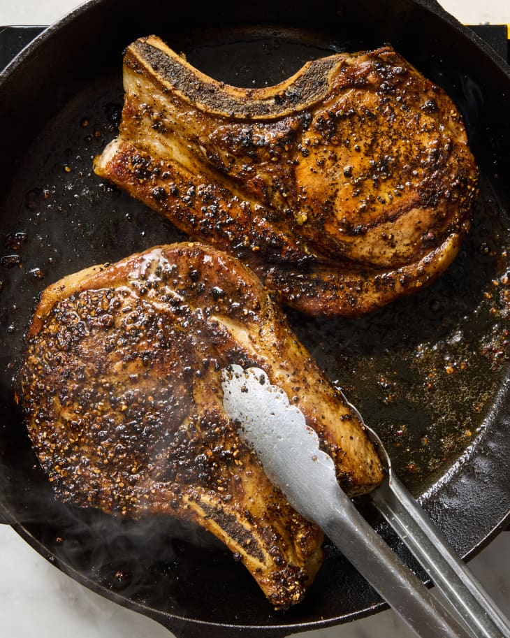 overhead shot of two pork chops being cooked in a cast iron.