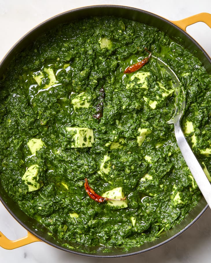 A pot of saag paneer on a marble surface with a large spoon in it.