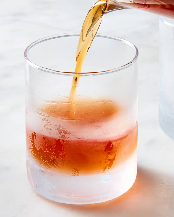 head on shot of a sazerac being poured in a small rocks glass garnished with a lemon peel.