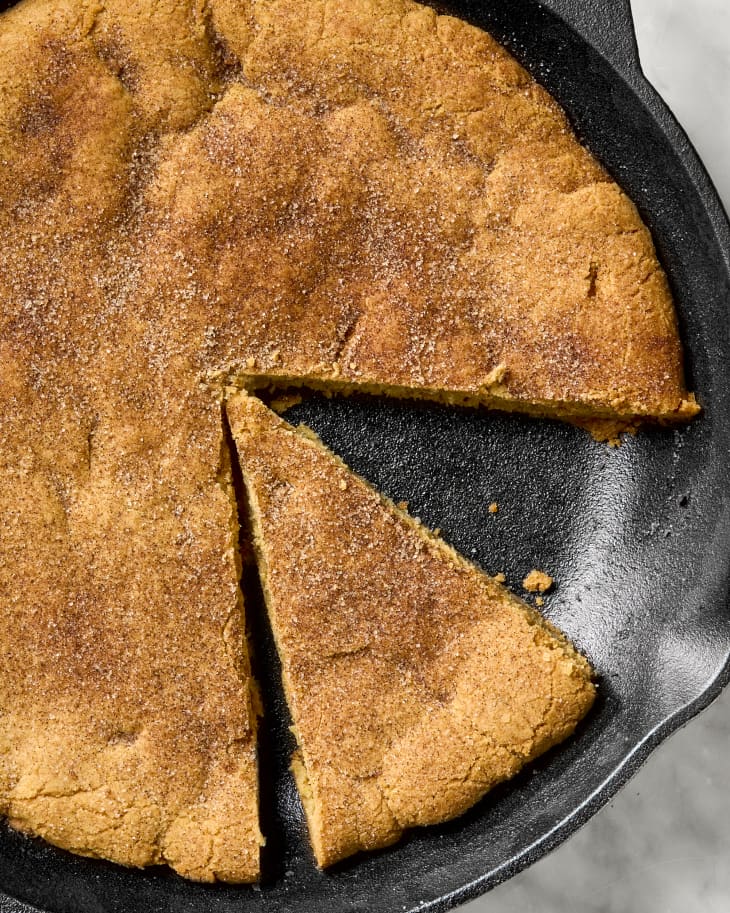 overhead shot of the snickerdoodle cookie in a cast iron skillet, with one slice taken from it, and another cut.
