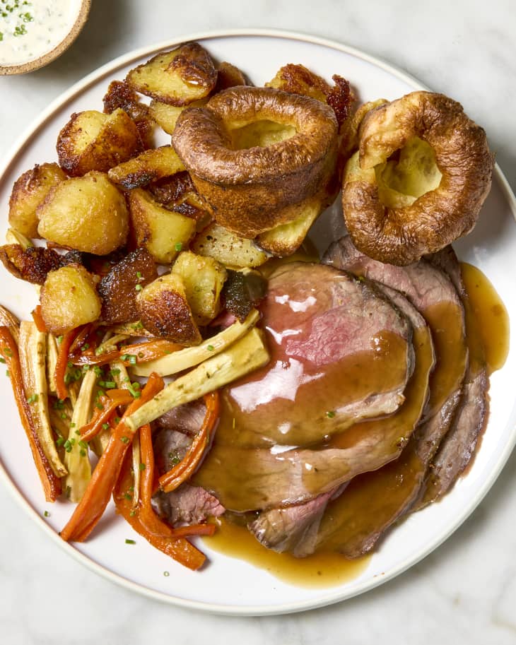 overhead shot of  white plate with roast beef, roasted carrots, crispy potatoes and yorkshire pudding.