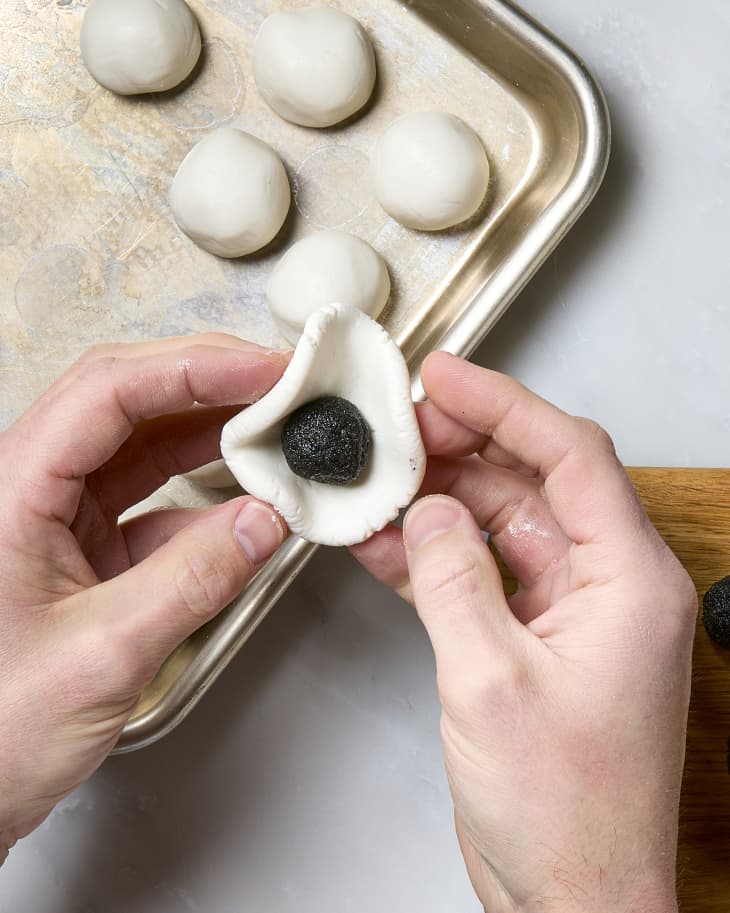 Two hands folding dough around a sesame paste filling for tang yuan.