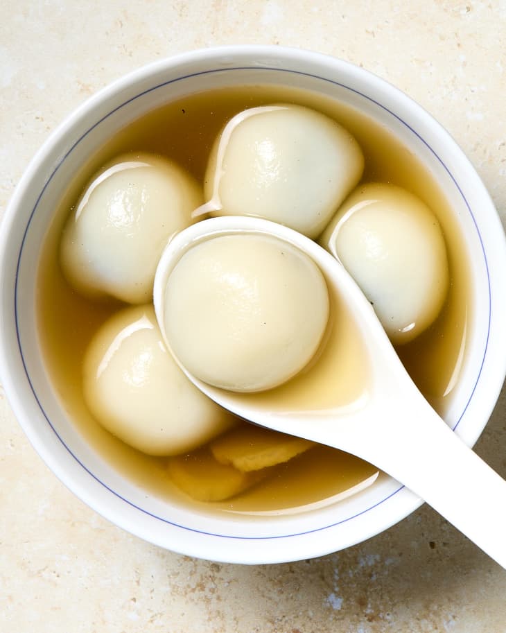 Bowl of tang yuan dessert rice balls stuffed with sesame paste in a sweet broth with one on a spoon.
