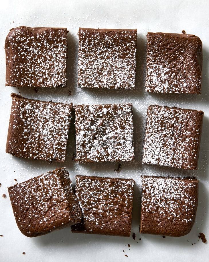 Overhead photo of cut brownies topped with powdered sugar on parchment paper.