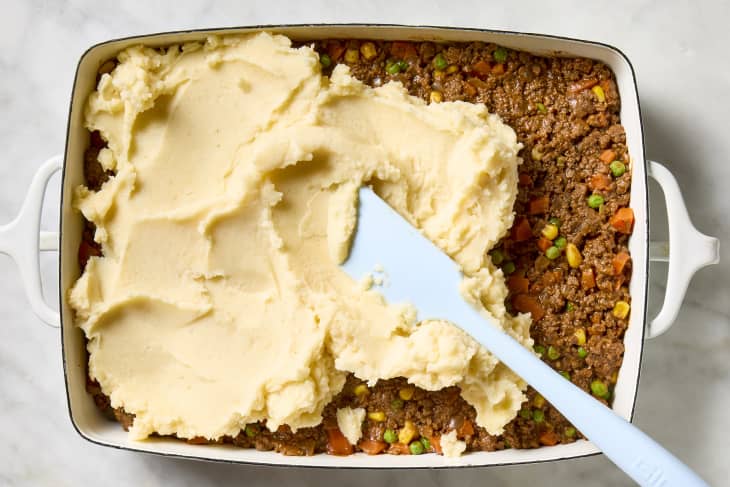 overhead shot of mashed potatoes being spread across the shepards pie filling