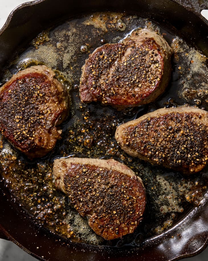 An overhead view of steak au poivre cooking in a cast iron skillet.