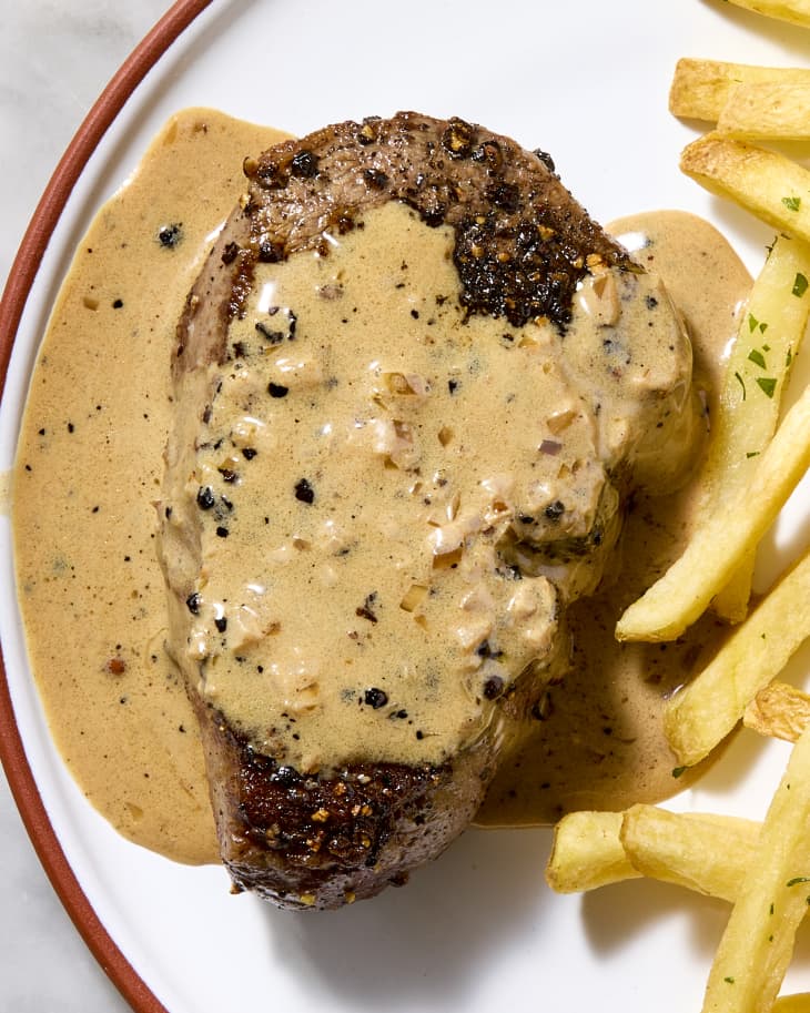 An overhead view of a filet of steak au poivre with french fries on a plate on a marble surface.
