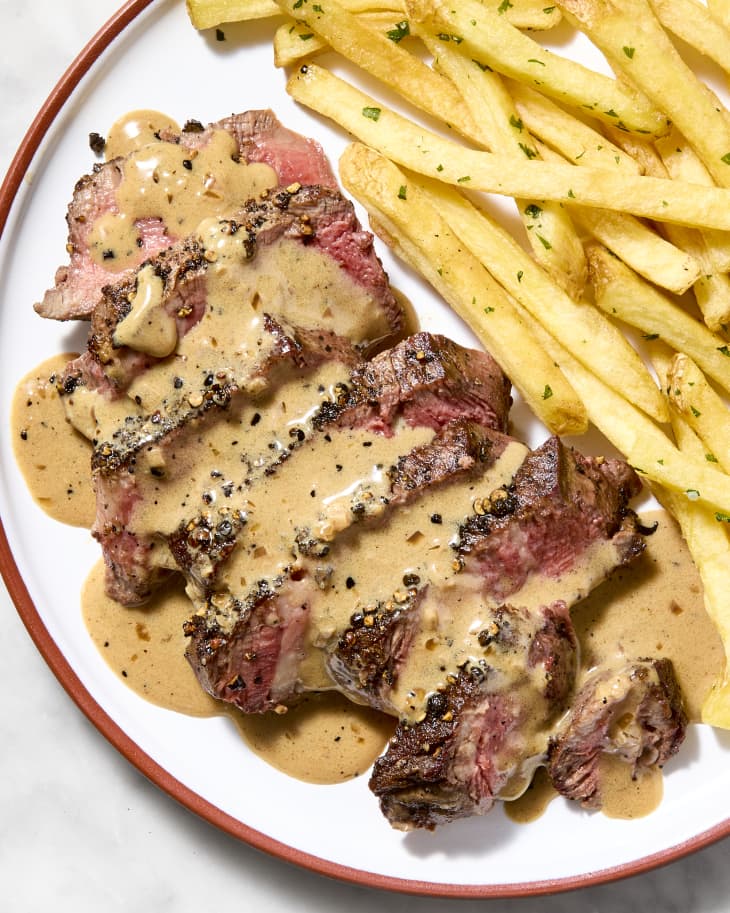 An overhead view of sliced steak au poivre with french fries on a plate on a marble surface.