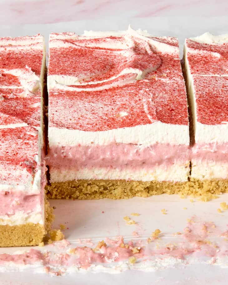 angled shot of no bake strawberry dream bars on parchment paper, showing all the layers of the bars.
