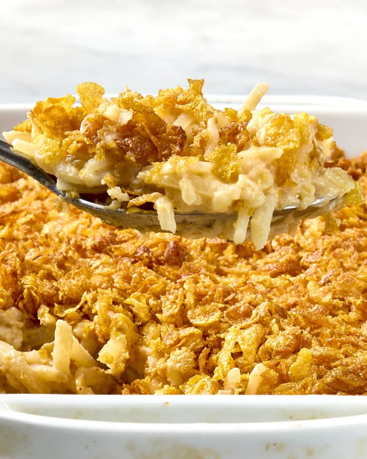head on shot of funeral potatoes in a white casserole dish, with a large scoop being taken from it