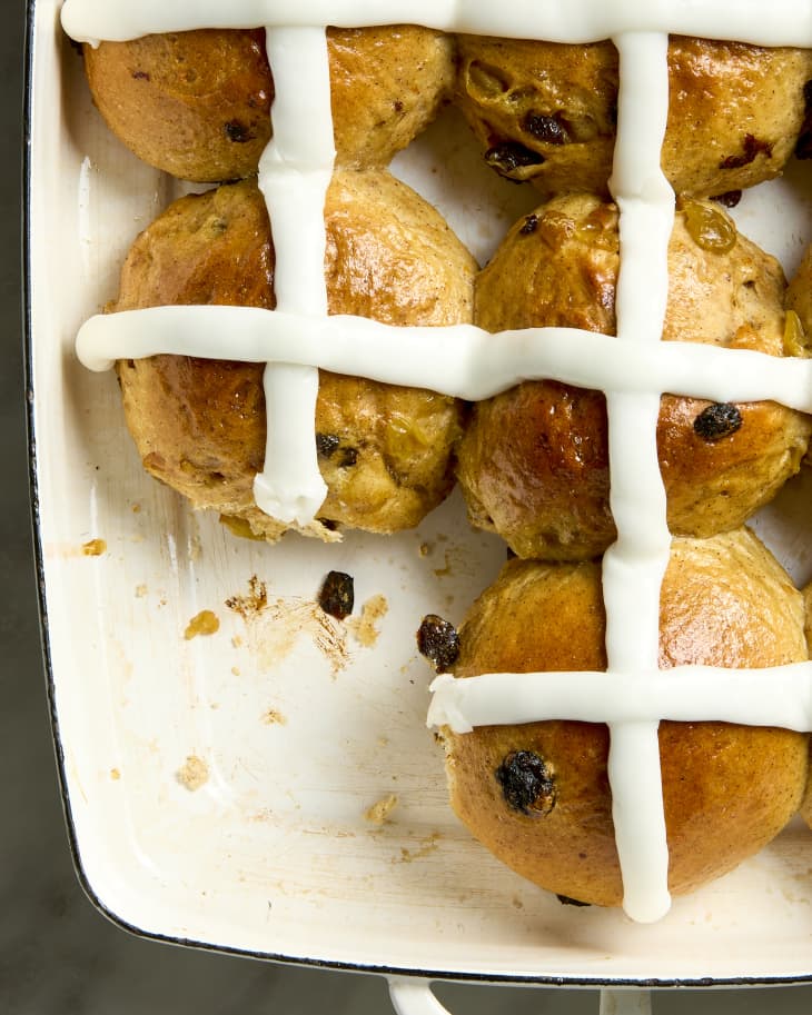 overhead shot of hot cross buns in a white baking dish with one missing in the bottom right of the dish.