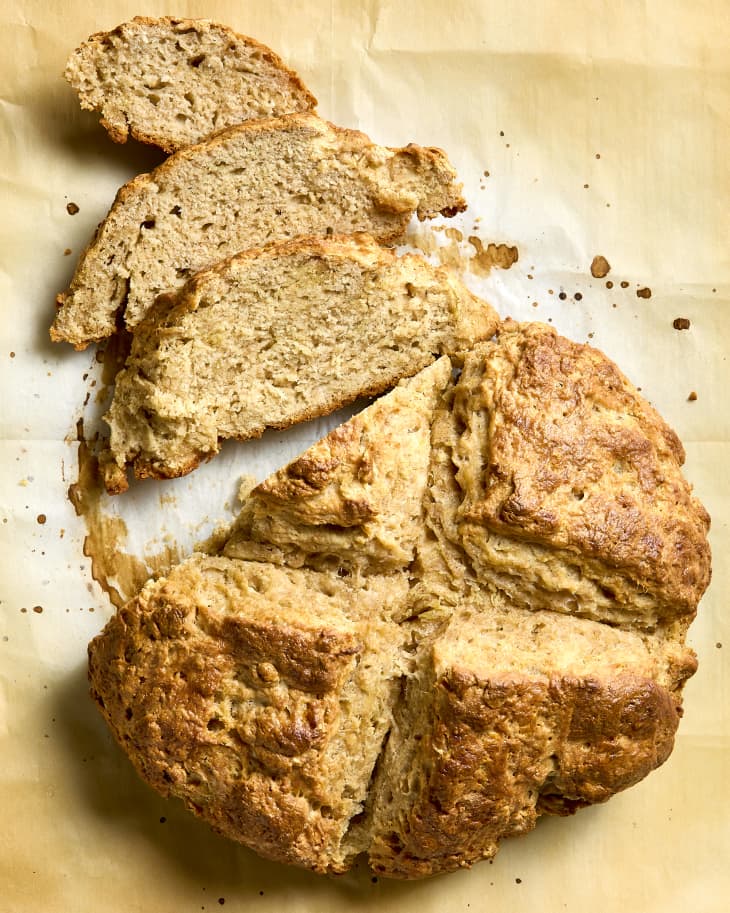 overhead shot of irish soda bread on parchment paper, with three slices resting in front of the loaf.