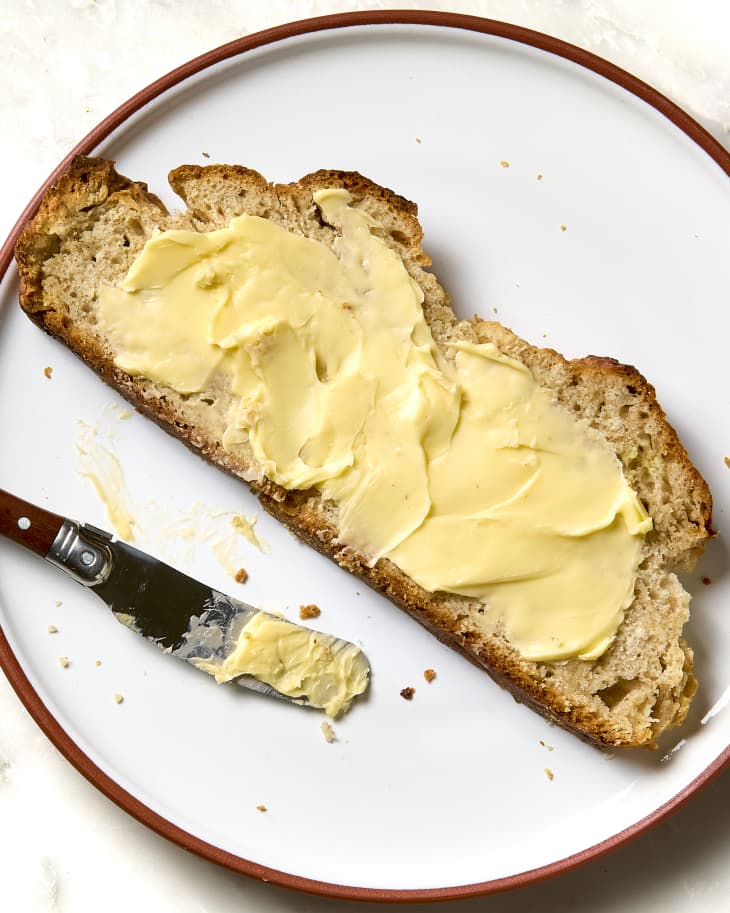 overhead shot of a slice of irish soda bread on a small white plate, with a thick layer of butter.