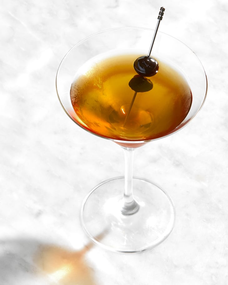 angled shot of a single manhattan in a martini glass, on a marble surface.