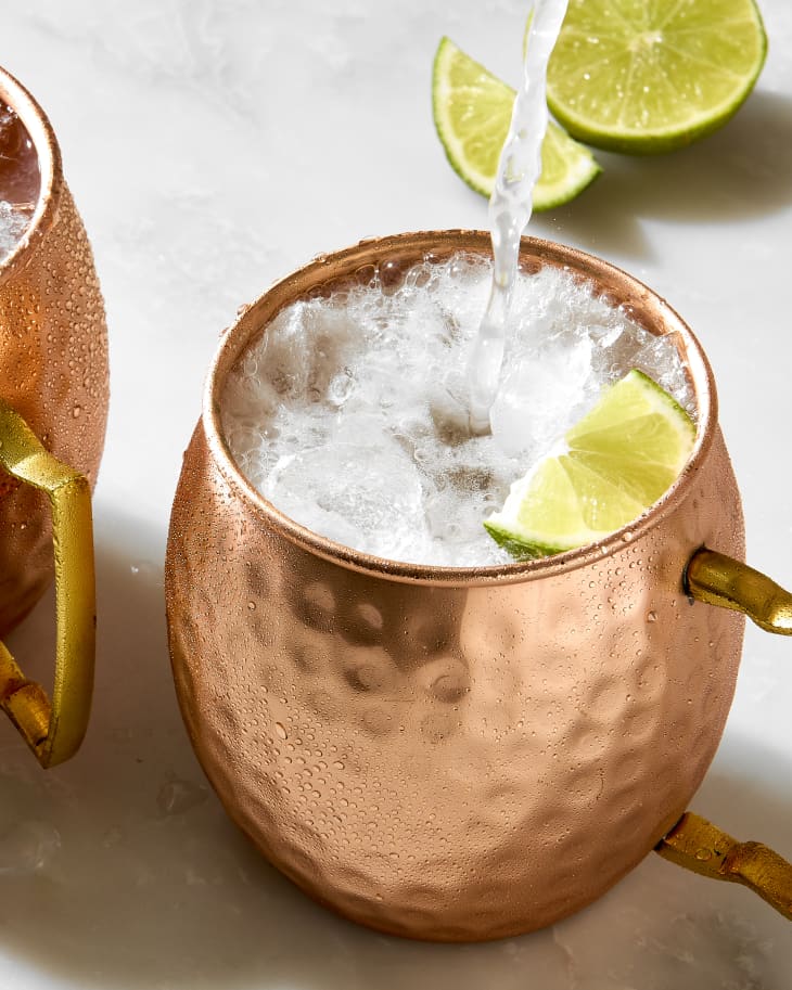 overhead shot of a moscow mule being poured into a copper mug, with a lime to the left of the mug.
