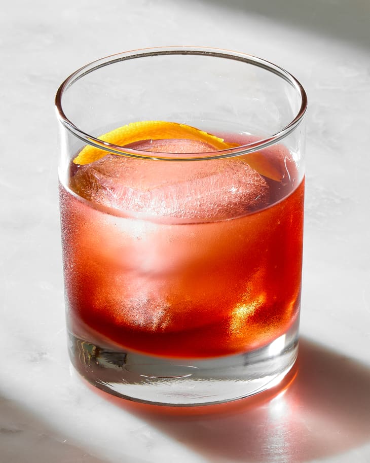 single negroni in a rocks glass, garnished with an orange peel inside of the glass.