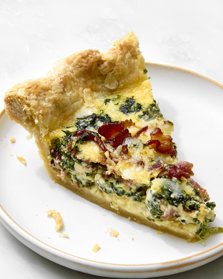 angled shot of a single slice of quiche on a small white and beige trimmed plate.