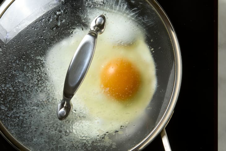 overhead shot of a fried egg being cooked with the pan lid on.