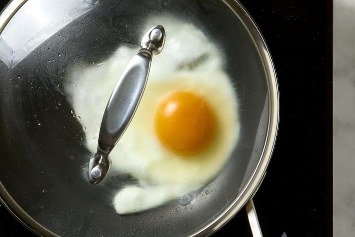 overhead shot of a fried egg being cooked in a pan with the lid on.