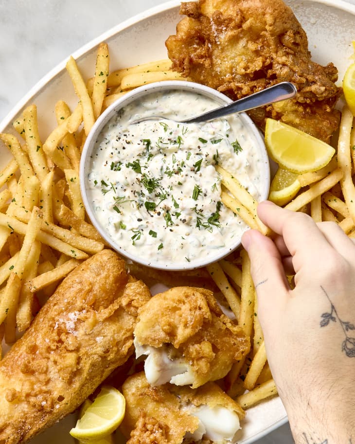 overhead shot of someone dipping their fries into tartar sauce on the platter.