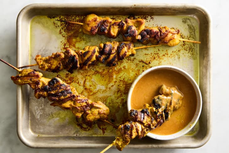 peanut sauce being lifted up by a spoon with chicken skewers near it