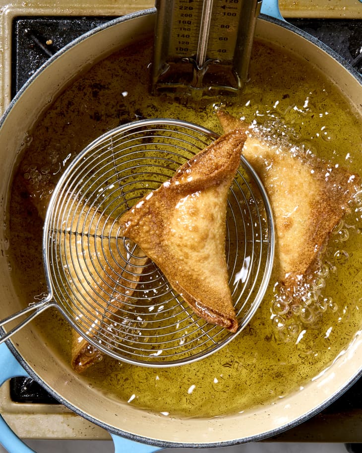 Overhead shot of a freshly fried crab rangoon being scooped out of a blue pot of hot oil.