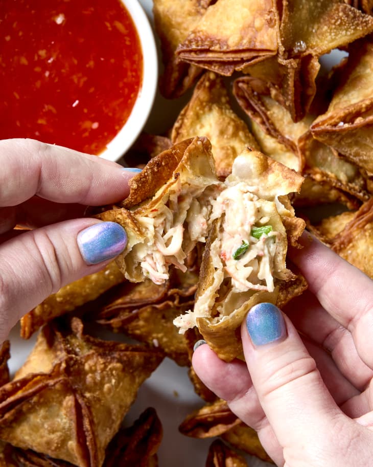 overhead shot of two hands pulling apart a crab rangoon to show the inside texture.