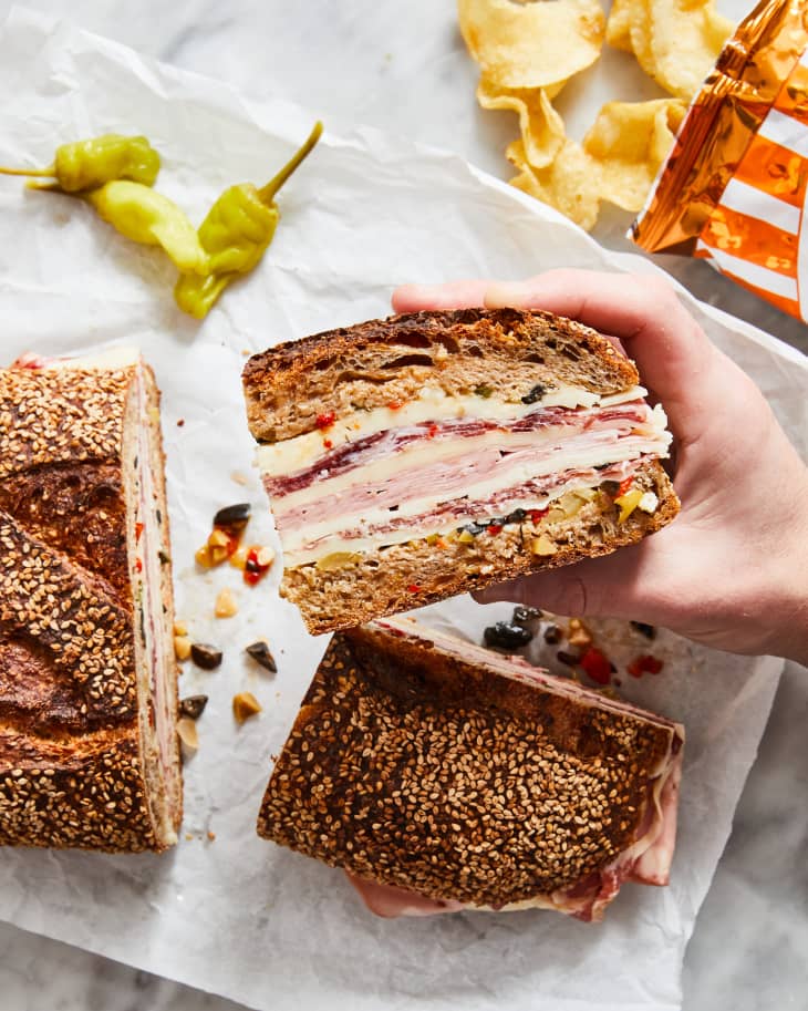 muffuletta on cutting board with hand holding it up