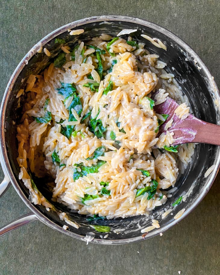 creamy spinach orzo in a pan with a wooden spoon