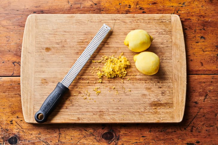 microplane, lemon zest, and 2 lemons on a cutting board