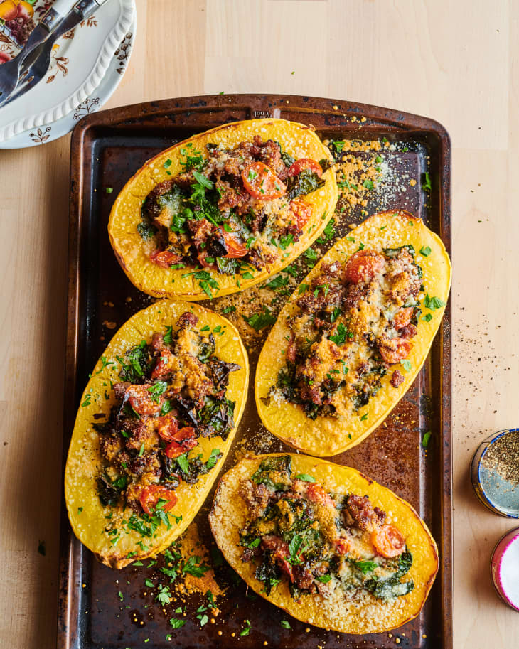 spaghetti squash halves filled with sausage, kale, and tomatoes on a baking sheet