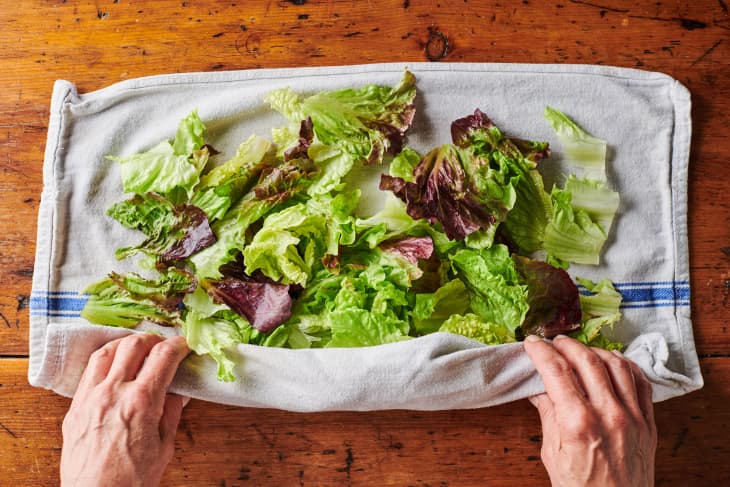 freshly washed salad greens are being wrapped in a kitchen towel in order to try the greens.